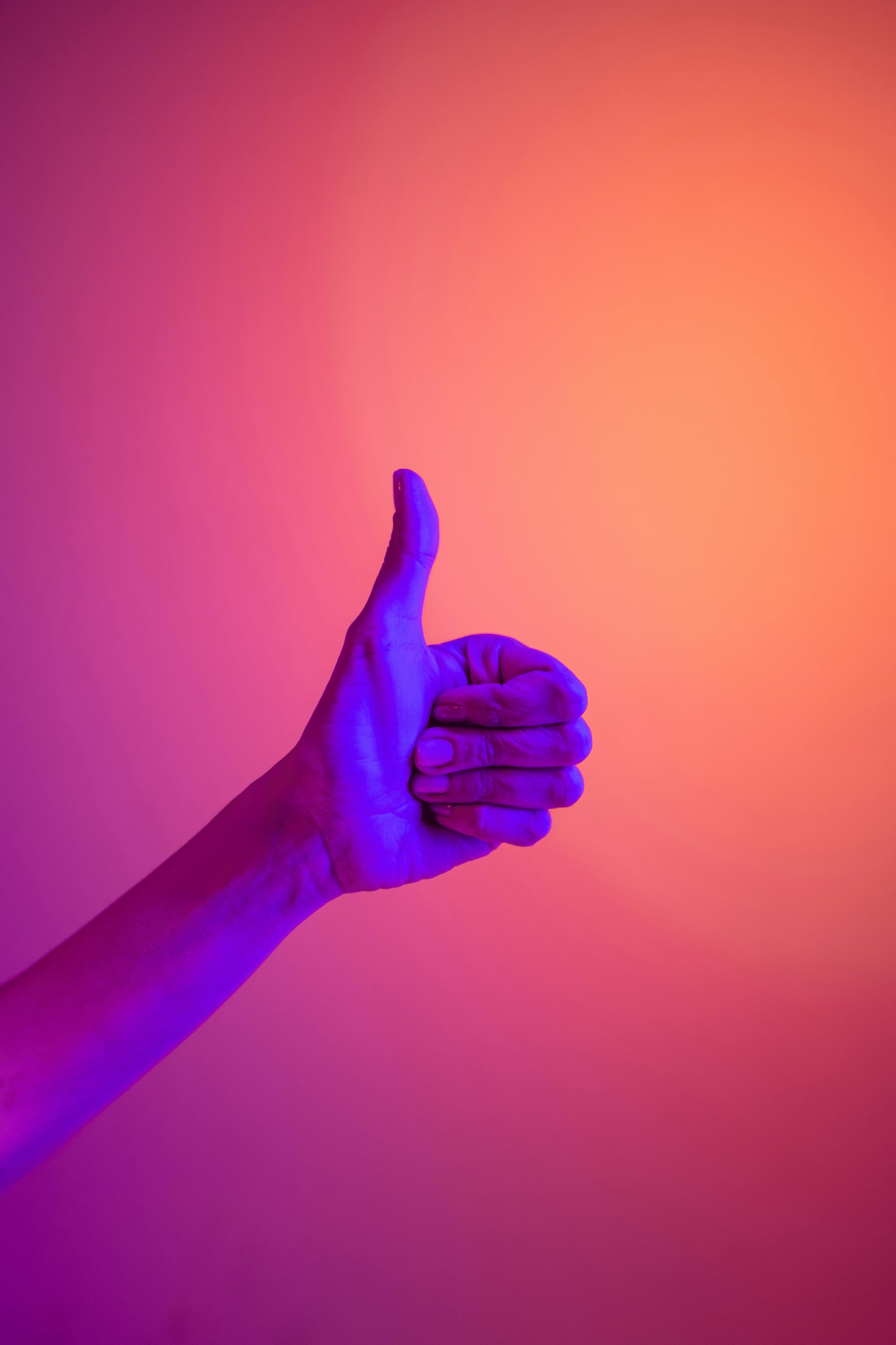 Hand giving a thumbs-up against a pink and orange background